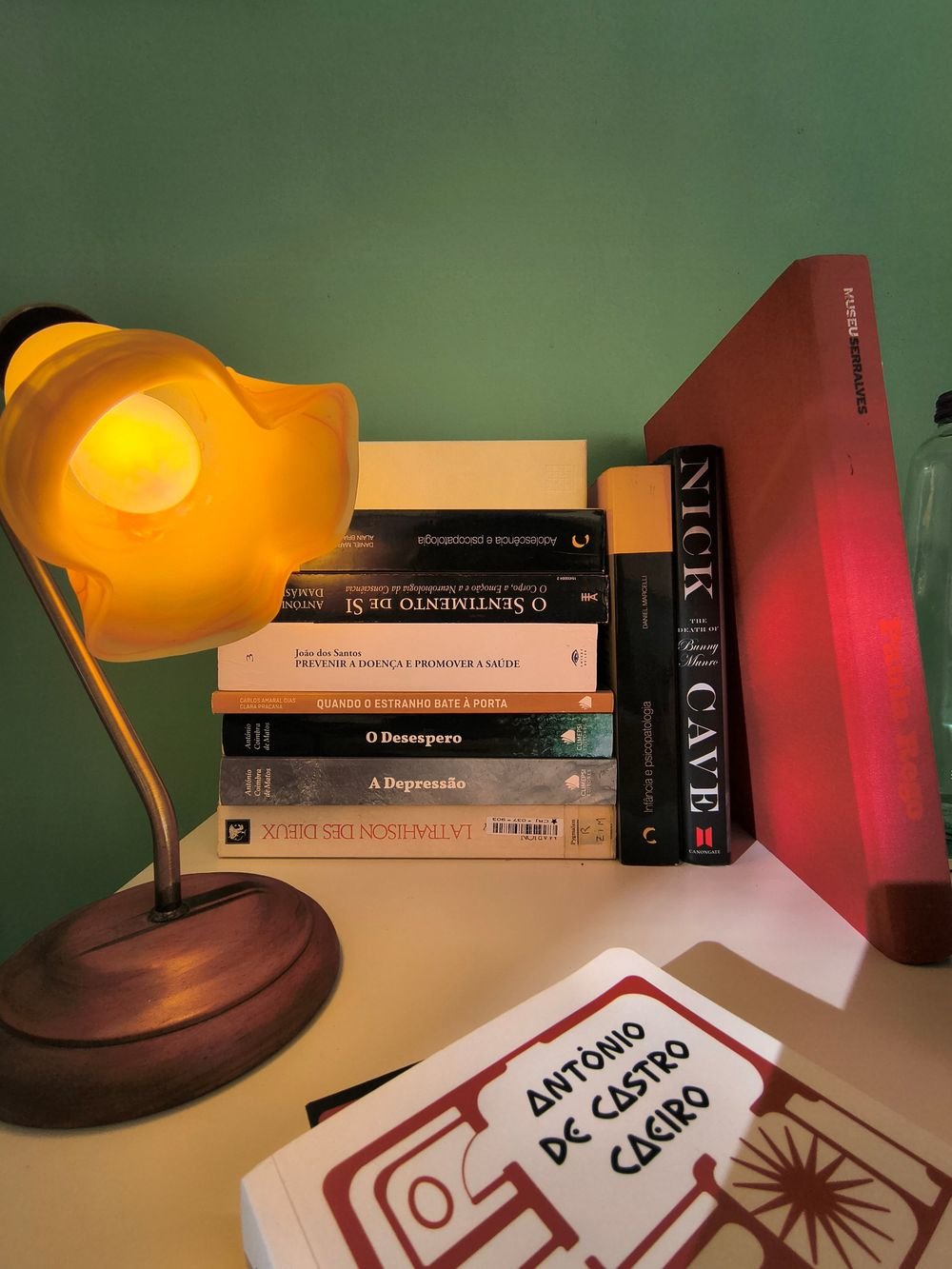 Candeeiro aceso junto a uma pilha de livros, contra a parede verde